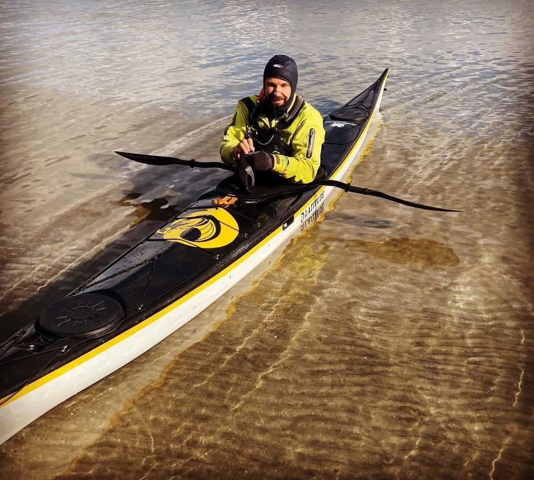 A sea kayaker sitting in a kayak in clear, shallow water